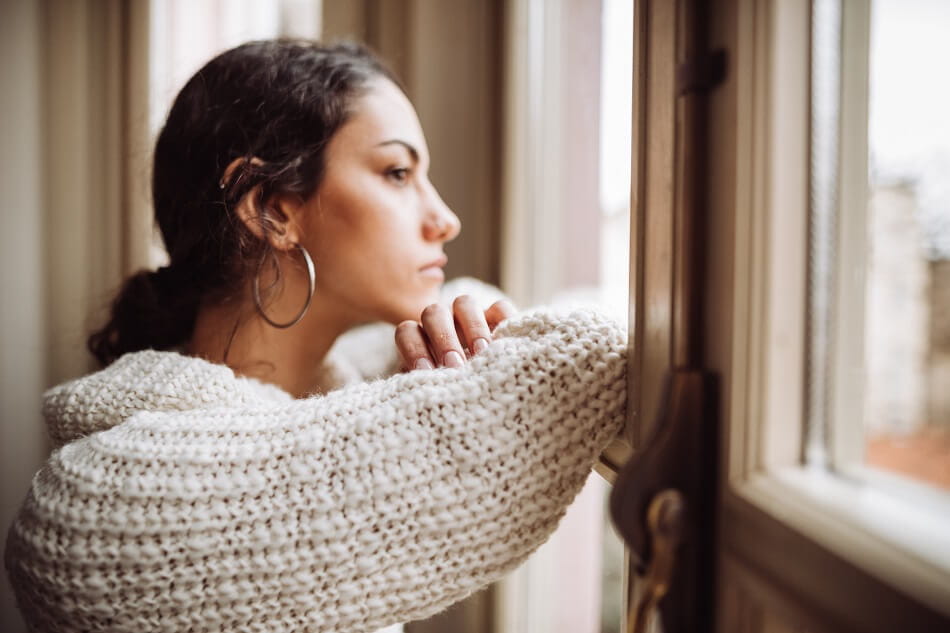 Millennial woman in a sweater looking out the window while thinking about finances