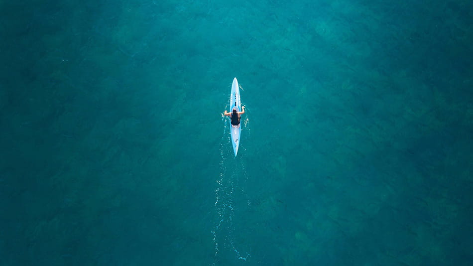 Ariel view of rower on clear blue waters symbolizing a long financial road ahead.