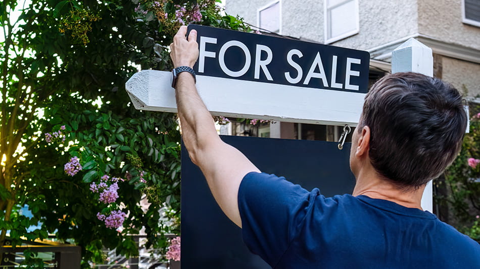 Man putting for sale sign up in front of his house