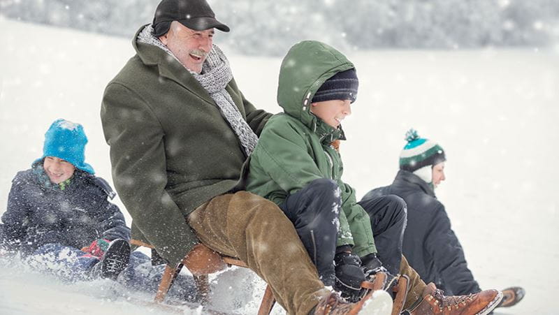 grand parent riding a sled with grand child because they planned ahead to avoid overspending at Christmas time. 